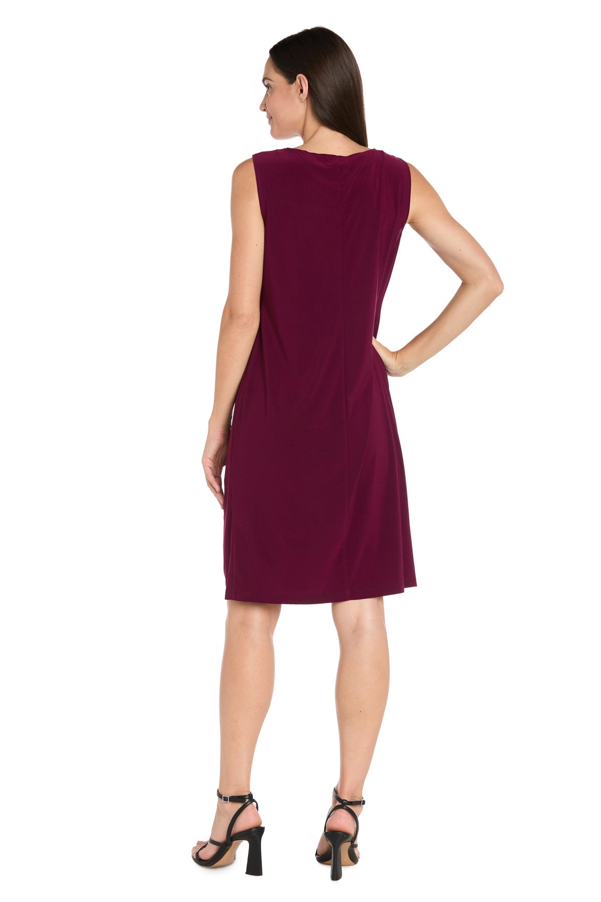 A woman with long brown hair stands with her back to the camera against a white background, modeling the Petite Short Wine Party Dress: R&M Richards 3029P and black heeled sandals.